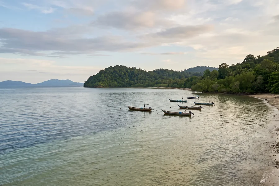 A mainland coastline in late afternoon light, shallow water in front and low islands on the horizon.